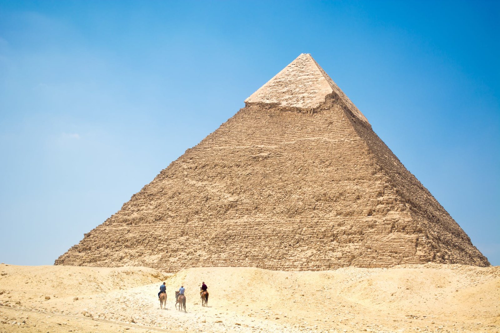 people riding a camel near pyramid under blue sky