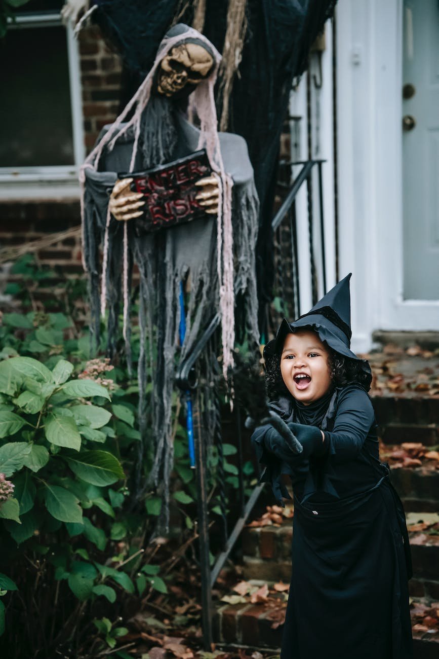joyful girl in witch costume standing near halloween decorations